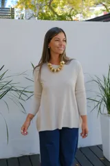 Sweater de tejido de punto en color beige, con cuello redondo, mangas tres cuartos y corte holgado con ruedo ligeramente más largo en la parte posterior.