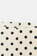 Vestido corto color crema con estampado de lunares negros. Presenta cuello redondo con lazada en la parte trasera, escote cuadrado, manga corta y cierre de cremallera oculta en la espalda.