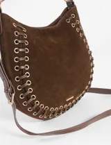 Cartera de hombro tipo hobo color verde claro, confeccionada en gamuza sintética. Presenta detalles de ojales metálicos plateados en los laterales y la base, entrelazados con tiras del mismo material, y una única asa corta para el hombro sujeta por argollas metálicas.