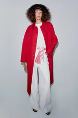 Trench largo color rojo de la línea ZW Collection de Zara, con cuello solapa, manga larga y bolsillos laterales ocultos. Presenta un diseño con forro interior a contraste y cierre frontal con botones a presión.