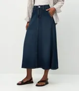 Pollera midi de corte evasé confeccionada en denim de algodón. Presenta un diseño clásico con trabillas en la cintura, cierre frontal con botón y cremallera, bolsillos funcionales y costuras verticales decorativas que realzan la silueta.