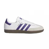 Championes Adidas modelo Samba ADV, con diseño clásico de perfil bajo. Presenta una base de cuero blanco con las icónicas tres tiras laterales y detalle en el talón en color violeta. Incluye puntera reforzada de gamuza en tono gris claro y suela de goma color marrón.