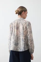 Camisa de manga larga con cuello con volados y botones nacarados. Presenta un estampado romántico de inspiración barroca en tonos azul y beige.