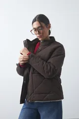 Campera acolchada de nylon color negro, con cuello alto, cierre frontal y botones a presión. Presenta un diseño de rombos y forro interior suave.