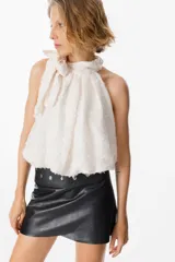 Blusa blanca sin mangas con cuello halter y lazo lateral. Confeccionada en tela de gasa con textura floreada en relieve.