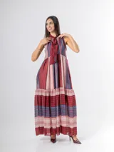 Vestido largo de corte halter en organdí, con estampado de rayas verticales y horizontales en tonos bordó, azul y crudo. Cuenta con un lazo en el cuello y un volado en la parte inferior.