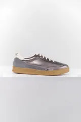 Zapatillas deportivas plateadas con detalles en gamuza gris, cordones blancos y suela color caramelo.