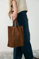 Bolso tipo tote de cuero gamuzado color tostado, con diseño de doble asa y cierre mediante cordón ajustable en la parte superior.