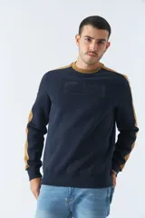 Buzo de felpa azul marino con cuello redondo y puños. Tiene mangas largas y calce regular. Presenta un logo estampado en relieve en el pecho y un logo de goma en la manga.