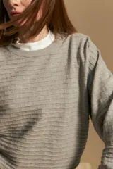 Sweater color crema con mangas abullonadas y puños elastizados. Presenta una textura tejida en relieve con patrón de ladrillos en el cuerpo y rayas horizontales en las mangas.