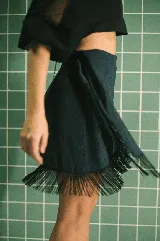 Falda tipo pareo corta, color azul metalizado con acabado brillante y flecos negros decorativos en el borde. Ajustable en la cintura.