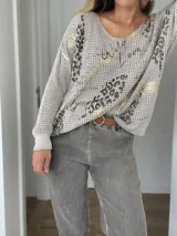 Buzo de tejido de punto con cuello redondo, manga larga y diseño holgado. Presenta un estampado con motivos de animal print y detalles en color dorado sobre una base de color beige.
