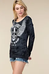 Remera manga larga de color negro con efecto gastado, escote redondo y un gran estampado frontal de una calavera con casco y alas, acompañada de inscripciones temáticas de estilo motero.