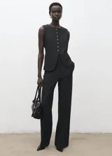 Chaleco de estilo sastre en color negro, con cuello redondo, cierre frontal de botones y diseño recto sin mangas.