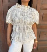 Blusa a cuadros crema con bordado floral tono sobre tono, cuello alto con volado, mangas cortas abullonadas, frunces frontales y lazos laterales regulables.