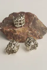 Anillo de diseño abierto con estructura de rejilla entrelazada, elaborado artesanalmente en metal con acabado plateado.