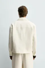 Sobrecamisa marrón de corte boxy fit en tejido compacto, con cuello solapa, manga larga con puños abotonados, bolsillos frontales de parche y cierre central de botones.