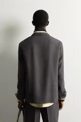 Blazer cruzado de corte relaxed fit, confeccionado en mezcla de lana de color marrón oscuro jaspeado. Presenta solapas de muesca, doble botonadura frontal multiposición y bolsillos con solapa en la cadera.