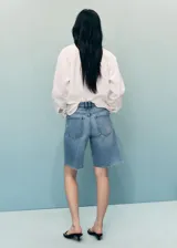 Short de jean de tiro medio con diseño recto, cinco bolsillos y bajo deshilachado. Cuenta con cierre delantero de cremallera y botón.
