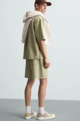 Bermuda de algodón color blanco, de corte relajado (relaxed fit), con cintura elástica ajustable mediante cordón. Posee bolsillos laterales y un bolsillo trasero de plastrón. Presenta un bordado en contraste en la pernera.