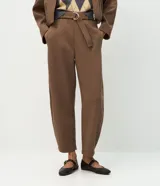 Pantalón de corte barrel, color marrón, confeccionado en algodón con felpa. Presenta cintura alta con cinto aplicado y hebilla metálica, y piernas de diseño amplio y cónico hacia los tobillos.