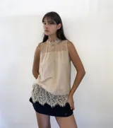 Musculosa de encaje color beige con cuello alto y diseño sin mangas. Presenta detalles de encaje floral y terminaciones con bordes festoneados en el ruedo.