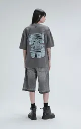 Remera de algodón premium color gris concreto, con corte oversize, hombros caídos y cuello redondo. Presenta un estampado frontal con las siglas "KM" y el texto "#KILOMBITOMAL" debajo en color celeste pálido.