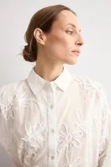 Camisa celeste con apliques florales bordados, cuello camisero, manga larga y cierre frontal de botones.