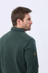 Buzo de felpa color verde oscuro, con cuello tipo polo, cierre frontal parcial con botones y bolsillos laterales. Presenta puños y ruedo acanalados.
