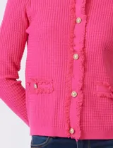 Cardigan de punto color fucsia, con escote a la base, cierre frontal con botones metálicos dorados y terminaciones desflecadas. Presenta bolsillos simulados en la parte delantera y mangas largas.
