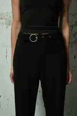 Pantalón de vestir negro de corte recto y tiro alto, con cinturón incorporado que presenta una hebilla metálica circular.