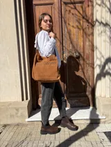Cartera tipo tote bag de cuero color camel, con detalles de tachas metálicas en el bolsillo frontal y tiras largas para el hombro.