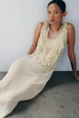Vestido largo color beige de viscosa, con escote cuadrado, tirantes anchos, detalles drapeados, volantes y aplicaciones de encaje a contraste en el pecho. Cuenta con cierre trasero de botones.