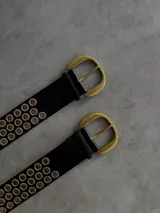 Cinturón negro de cuero ecológico con hebilla metálica dorada y doble hilera de ojales dorados a lo largo de toda la tira.