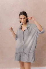 Vestido camisero corto de denim liviano azul con efecto desgastado, de corte oversize, con cuello camisero, botonadura frontal, bolsillo plaqué en el pecho, mangas largas y volado fruncido en el ruedo.