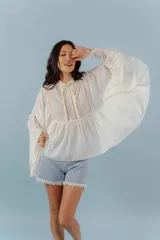 Camisa de algodón con diseño romántico, mangas amplias y detalles de puntillas verticales en el frente. Presenta un corte holgado y fluido.