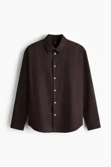 Camisa de manga larga color marrón, con cuello inglés, cierre frontal de botones, bolsillo en el pecho y bajo redondeado. Confeccionada en mezcla de algodón y lino.