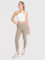 Calza deportiva de tiro alto con largo al tobillo, confeccionada en tejido elástico de color beige. Presenta un diseño minimalista sin bolsillos y un pequeño logo bordado en la cadera.