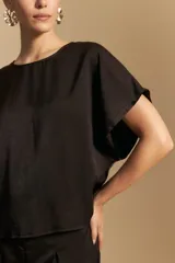 Top negro de manga corta tipo kimono, con silueta amplia y caída fluida. Confeccionado en un tejido liviano con leve brillo. Presenta un botón de nácar en la espalda con una pequeña abertura.