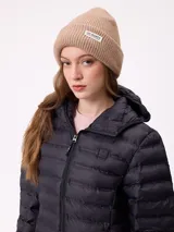 Gorro tipo beanie de tejido de punto acanalado en color beige, con doblez en el borde y etiqueta rectangular con el logo de la marca en la parte frontal.