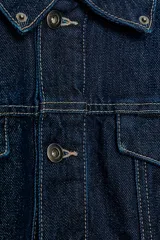 Cazadora de corte cropped confeccionada en tejido denim azul oscuro, con cuello solapa, cierre frontal de botones metálicos y bolsillos con solapa en el pecho. Presenta detalles de aplicación en piel a contraste en la zona de los hombros.
