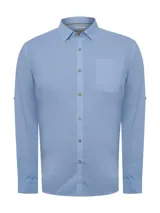 Camisa de manga larga RKF modelo Galiton, confeccionada en popelina de algodón orgánico color azul. Presenta cuello camisero, cierre frontal con botones de madera, bolsillo en el pecho con logo bordado y mangas ajustables.
