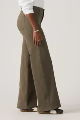 Pantalón de jean estilo wide leg en color verde oliva, con costuras verticales frontales que recorren el largo de las piernas. Presenta un diseño de tiro medio con cierre de botón y cremallera, y bolsillos laterales.