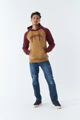 Buzo canguro gris con mangas ranglan azul marino, capucha con cordones ajustables y bolsillo delantero. Estampado frontal con el logo de la marca y el año de fundación.