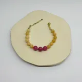 Pulsera elástica con cuentas de jade amarillo y jaspe rosa, separadas por hilo rosado. Cierre de acero hipoalergénico con baño de oro.