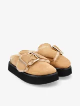 Zueco negro de cuero con plataforma y plantilla recubierta de piel de oveja. Presenta una hebilla dorada de gran tamaño en la capellada.