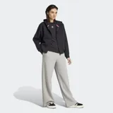 Pantalón Adidas de pernera ancha, color gris melange, confeccionado en suave tejido de felpa francesa. Cuenta con cintura elástica y el logo del trébol bordado en la parte superior delantera.