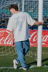 Remera de algodón de corte holgado, color blanco con cuello redondo en tono celeste claro. Presenta un pequeño bordado de la bandera de Uruguay en el pecho.
