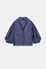 Camisa azul confeccionada en hilatura con 15% de lino. Tiene cuello solapa, escote pico, mangas 3/4 abullonadas, bajo recto y cierre frontal con botones.