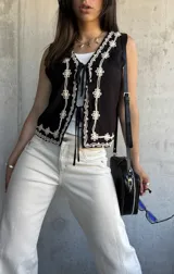 Chaleco negro con bordado de flores blancas, escote en V y lazos de ajuste en el frente.